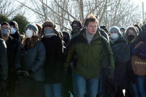 Mitch Emhoff (Matt Damon) stands in a crowd of masked civilians; the CDC now recommends wearing cloth coverings in public settings when social distancing cannot be maintained.
