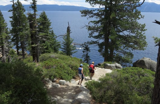 Two people hike down to a beach in Lake Tahoe. They are surrounded by the beauties of nature.