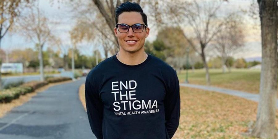 Robinson stands in the street, smiling, wearing an End the Stigma shirt encouraging people to open up about their mental health.