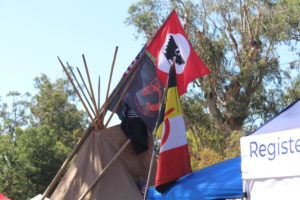 Atop an American Indian tipi flies several flags, including the United Farm Worker flag and a Prisoner of War/Missing in Action flag.
