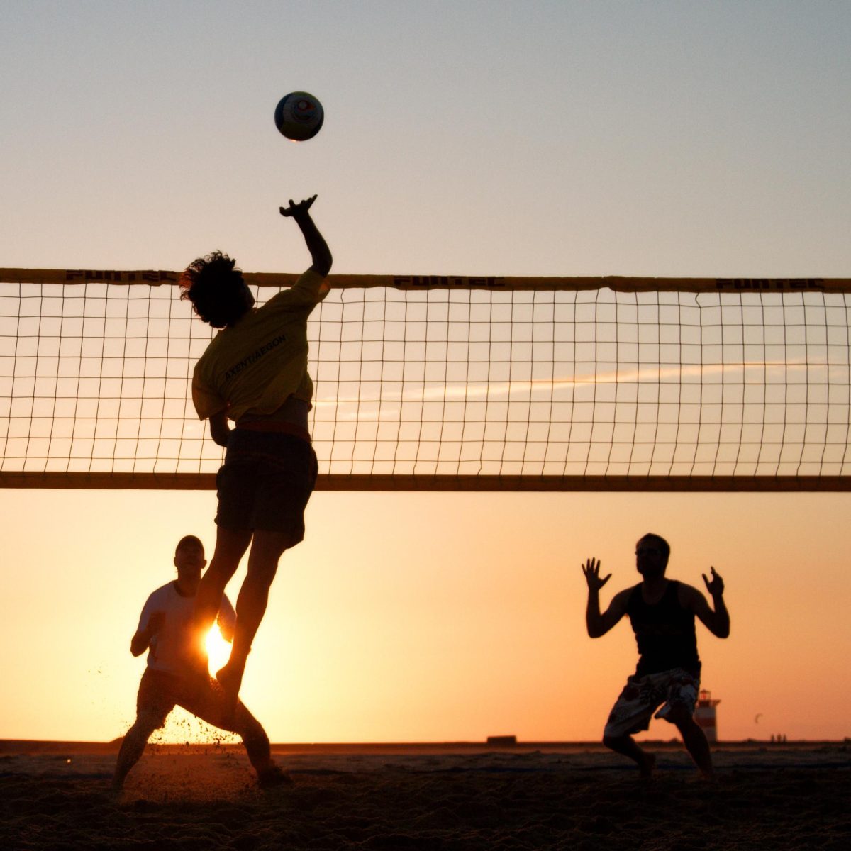Three boys playing volleyball for fun on a beach with the sunset in the background.