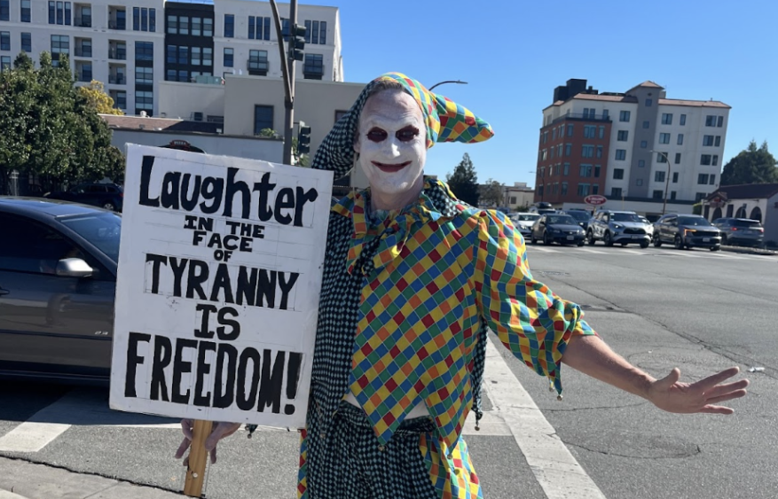 Protester Scott Hardman dressed up and posing with his sign 'Laughter in the face of tyranny is freedom!'