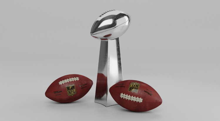 The Vince Lombardi Trophy sits next to two NFL footballs.