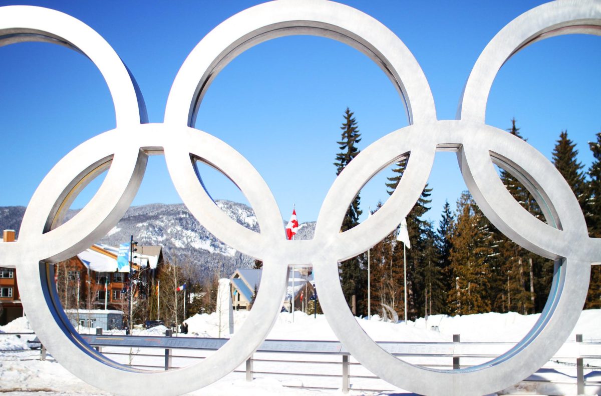 A view of the five olympic rings with a background of snowy hills lush forestry