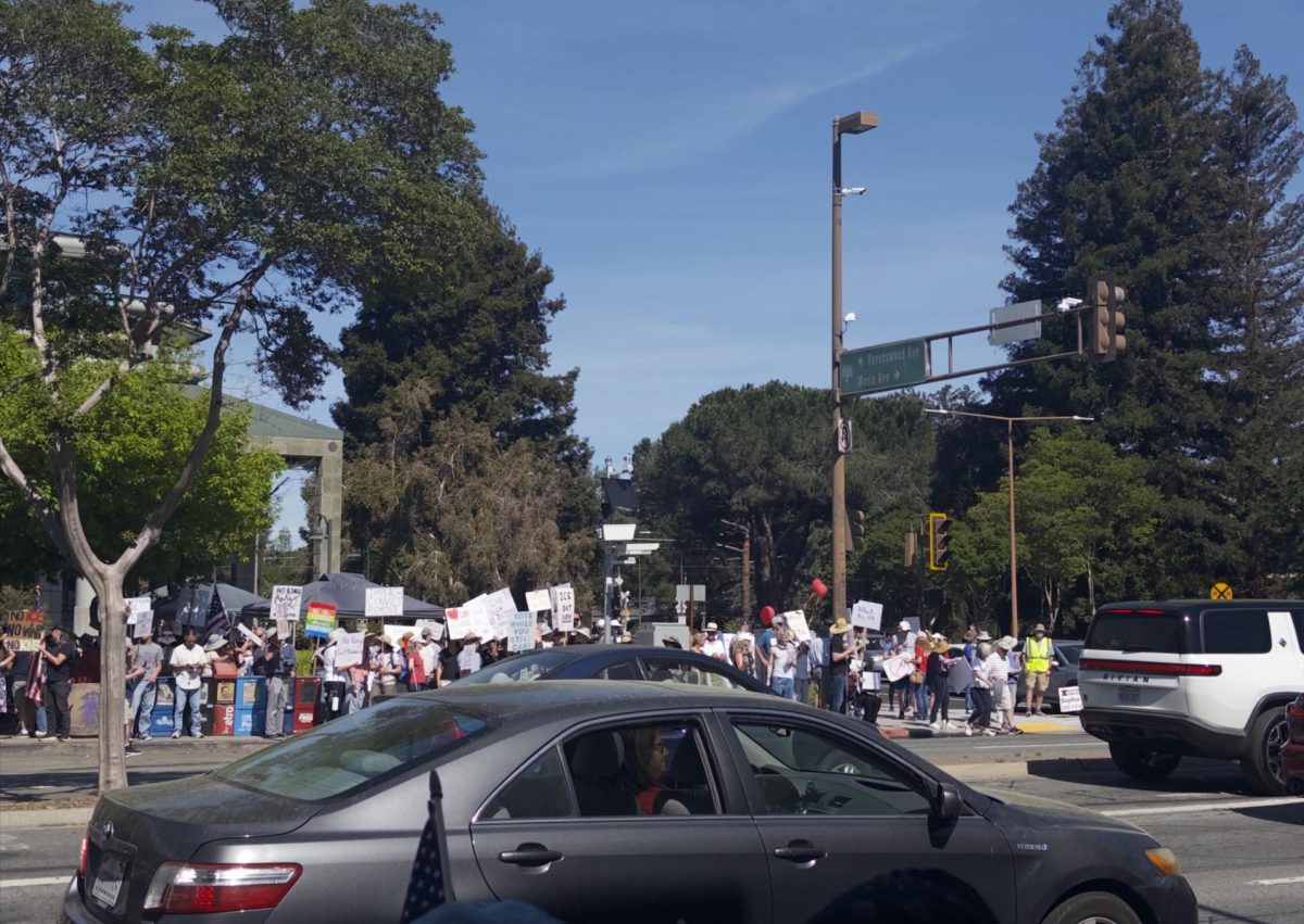 A crowd gathered on the sidewalk of El Camino Real in Menlo Park, holding signs with messages like “No Kings” and “ICE out.”